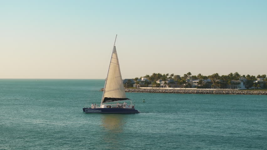 This breathtaking aerial view captures the beauty of Sunset Key Island in Key West, Florida, with its stunning turquoise waters and a picturesque sailboat sailing gracefully at sunset
