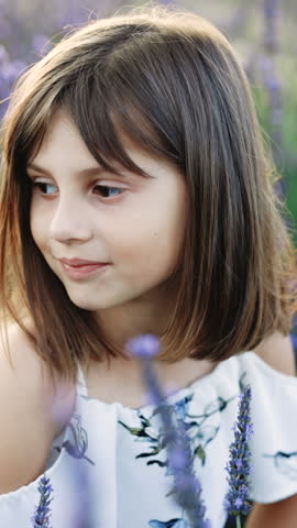 Vertical Format Video of Face of beautiful little girl with lavender. Aromatherapy. Natural cosmetic. Gentle perfume. Young little girl in a white dress through lavender field at sunset