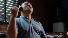Locked close up shot, middle-aged Asian man sitting on leather sofa in living room wearing headphone to listening music from tablet and singing a song with happiness - Powered by Shutterstock - Get 15% off with code: PIKWIZARD15