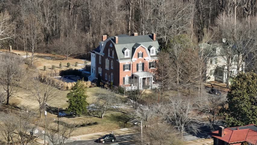 Colonial style houses with red brick and chimneys on sunny day in Virginia. Leafless trees in neighborhood. Aerial approaching shot. Symmetrical Facade with central door.Gabled roof with dormer window