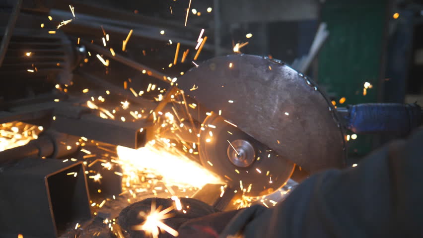 Hands of professional worker grinding metal. Circular saw sawing steel at industrial manufacture. Many bright sparks fly from hot metal. Saw cutting machine cut detail in garage. Slow motion Close up