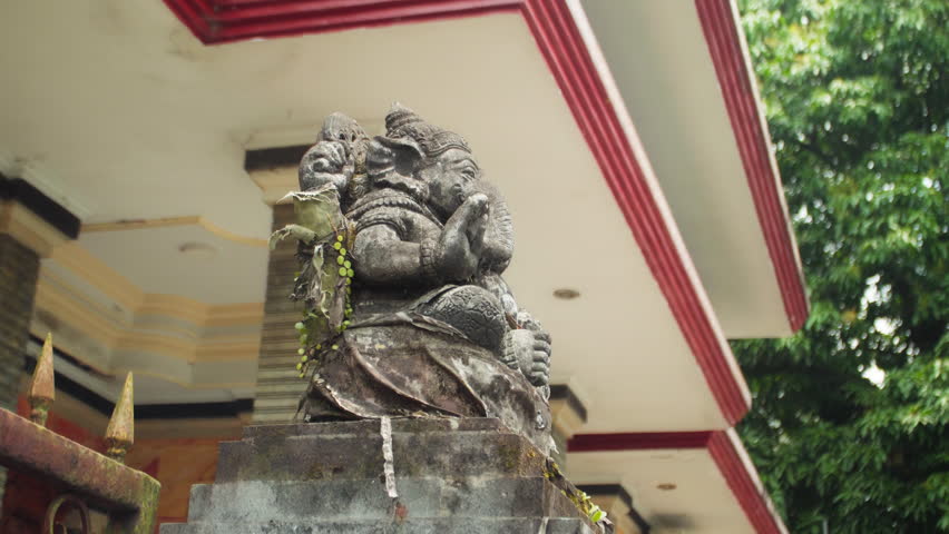 An old stone statue of Ganesha covered with moss, standing on the street