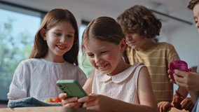 Smiling pupils browsing cellphone game enjoying school break closeup. Happy schoolgirl playing on smartphone with classmates in classroom. Joyful children interacting with mobile phone in class room. - Powered by Shutterstock - Get 15% off with code: PIKWIZARD15