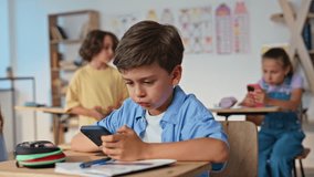 Children using gadgets in classroom at group activity. Students elementary school sitting desks playing at smartphones. Little pupils involved in cellphones screens at class. Kids phone addiction - Powered by Shutterstock - Get 15% off with code: PIKWIZARD15