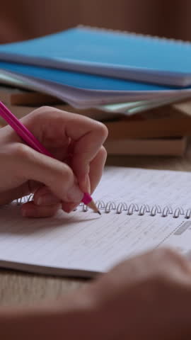 Close-up image of a young woman's hand taking notes and writing with a pencil in a notebook. Concept of pupils, students, studies, exams, tests, learning. Office table with books