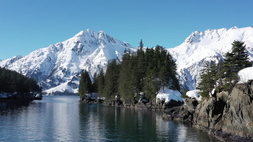 Aerial view of serene snowcapped mountains and a tranquil lake reflecting the clear sky, Chugach State and National Park, Alaska, United States.