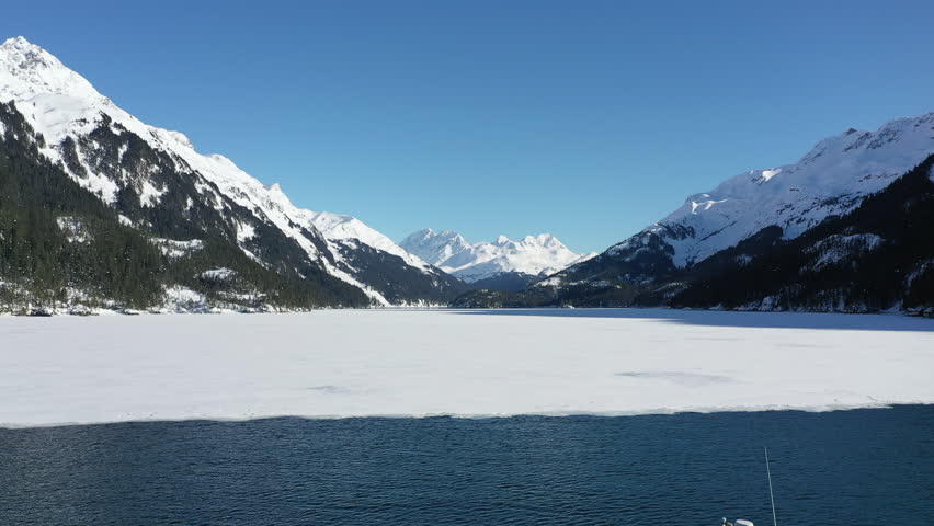 Aerial view of serene snowcapped mountains and a pristine lake with a boat, Chugach State and National Park, Anchorage, Alaska, United States.