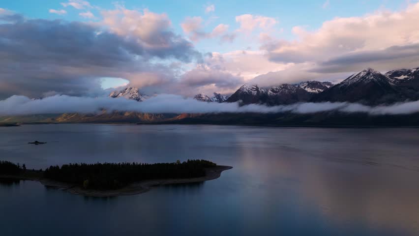 Aerial view of snowy mountains and serene forest with tranquil lake and islands at sunrise, Grand Teton, Wyoming, United States.