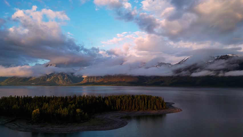 Aerial view of snowy mountains and tranquil forest surrounding a serene lake with islands at sunrise, Grand Teton, Wyoming, United States.