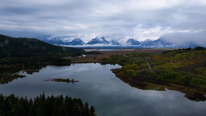 Aerial view of snowy mountains and serene forests surrounding a tranquil lake with islands at sunrise, Grand Teton, Wyoming, United States.