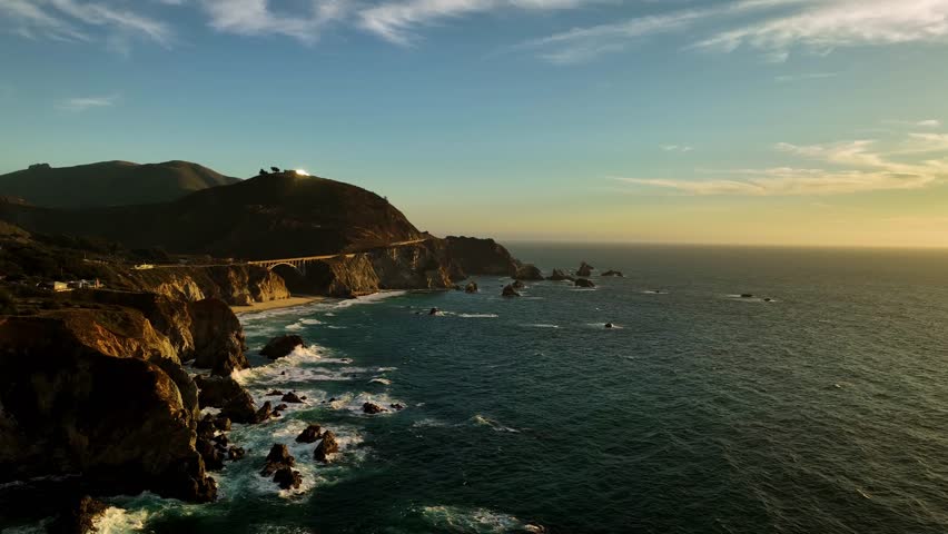 Aerial view of bixby creek bridge at sunset over the rugged coastline with crashing waves and clouds, Big Sur, California, United States.