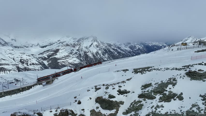 Aerial drone footage of Gornergrat bahn railway running towards summit station with Matterhorn mountain peak background in Zermatt on a sunny winter day. Swiss Alps, Switzerland travel journey trip