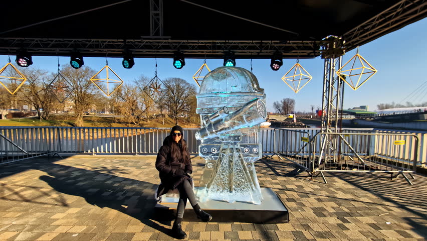 Woman posing by an astronomy telescope ice sculpture in Jelgava, surrounded by festival lights