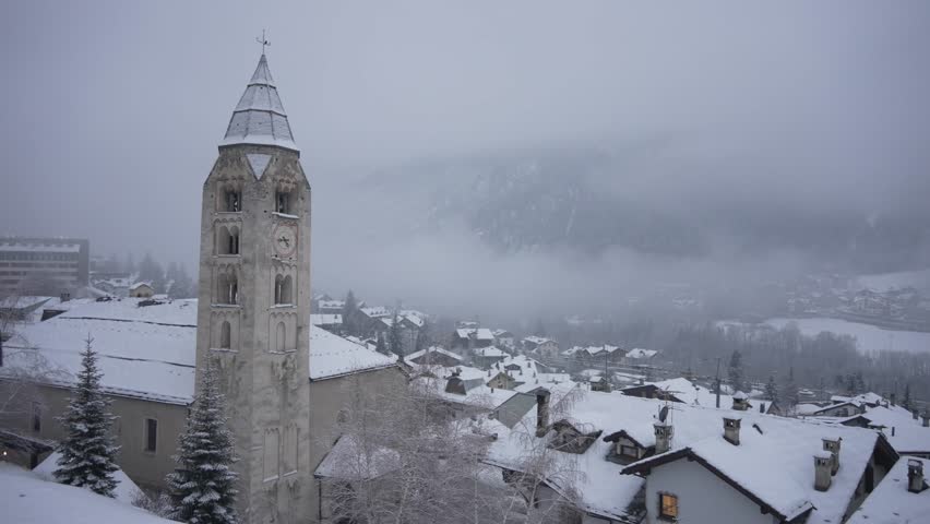 View of snow covered town centre and Church of Saint Pantalon in winter at dusk in Courmayeur, Aosta Valley, Italian Alps, Italy