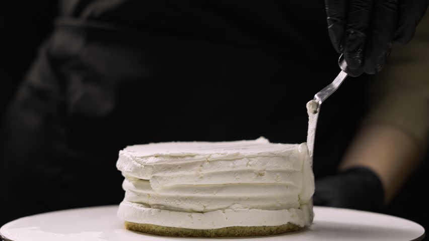 step by step process of making benta cake with banana filling. close-up of a pastry chef carefully smoothing the cream cheese on the side with a special spatula. step fifteen