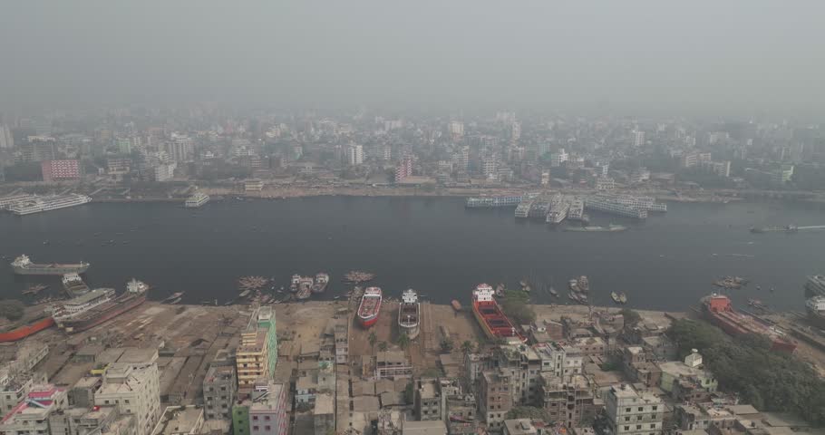 Aerial view of bustling shipyard and boats along Buriganga river with urban skyline and concrete buildings, Sadar Ghat, Dhaka Province, Bangladesh.