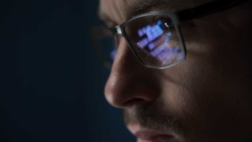 Close up of focused software engineer or data scientist wearing glasses, analyzing code on his screen. Programming script reflects on his eyeglasses as he works late. - Powered by Shutterstock - Get 15% off with code: PIKWIZARD15