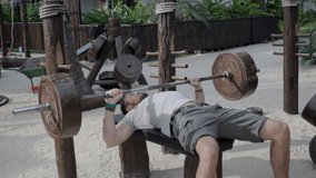 Caucasian male lifting weights, doing bench press, shoulder workout on the tropical thai beach in public outdoor gym. - Powered by Shutterstock - Get 15% off with code: PIKWIZARD15