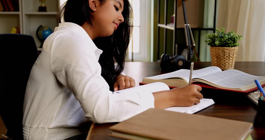 Indian Asian teenage girl studying at home, writing notes from a book, completing assignments or homework in a cozy lavish home, focused on education, exam preparation, and self-study in airy space