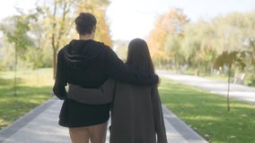 back view of a young couple embracing and talking as they walk through a beautiful autumn park. They enjoy each other company amid vibrant fall foliage and crisp air. - Powered by Shutterstock - Get 15% off with code: PIKWIZARD15