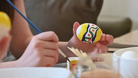 Close-up of child hands painting a colorful Easter egg with a brush. The egg has yellow, green, red and blue patterns. Cozy home interior, soft daylight. - Powered by Shutterstock - Get 15% off with code: PIKWIZARD15