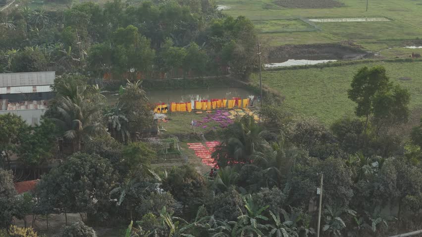 Aerial view of red clothes drying near a serene pond surrounded by lush greenery and fields, Dhaka, Dhaka, Bangladesh.