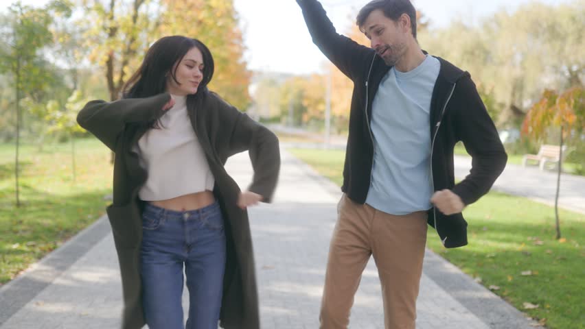 Amid the warm colors of autumn, a young couple dances in a park, enjoying a playful moment together. Their happiness and connection are evident in this sunny scene.