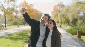 Two young Hispanic American or European men and women in love enjoy a fun fall moment in the park, taking a selfie, dressed in casual autumn clothing, happy and playful. - Powered by Shutterstock - Get 15% off with code: PIKWIZARD15