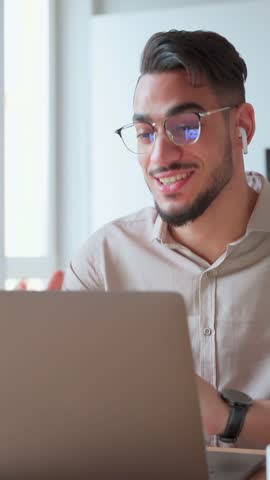 Young adult Indian businessman having business videocall with college at online conference meeting. Mature arabian smiling man student learning course using pc laptop webcam at home office. Vertical