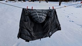 Black winter puffer coat with frost hanging on a clothesline in winter, swaying in the cold wind - Powered by Shutterstock - Get 15% off with code: PIKWIZARD15