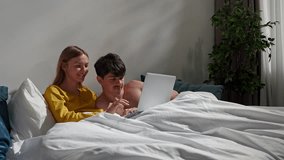 Couple relaxing together in bedroom at home, man and woman laying in bed and talking by video call on laptop, positive expression. Slow motion - Powered by Shutterstock - Get 15% off with code: PIKWIZARD15