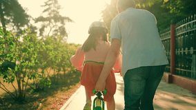 Dad teaches kid daughter to ride bike in park. Child cyclist with dad in nature park. Happy family little girl in helmet together with her dad learns to ride bicycle outdoors in summer. Family weekend - Powered by Shutterstock - Get 15% off with code: PIKWIZARD15