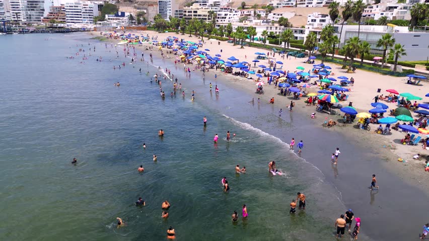 Peruvian beach shore alive with commercial activity and people enjoying the sun-drenched summer day.