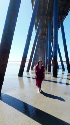 Young woman walking under rosarito beach pier wearing red dress