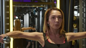 Beautiful blonde young woman with tattoos lifts dumbbells while performing exercises to strengthen her arm muscles in gym, with backdrop of backlighting. - Powered by Shutterstock - Get 15% off with code: PIKWIZARD15