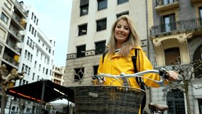 Confident young woman wearing yellow raincoat holding bicycle handlebars, posing in front of building in urban environment - Powered by Shutterstock - Get 15% off with code: PIKWIZARD15