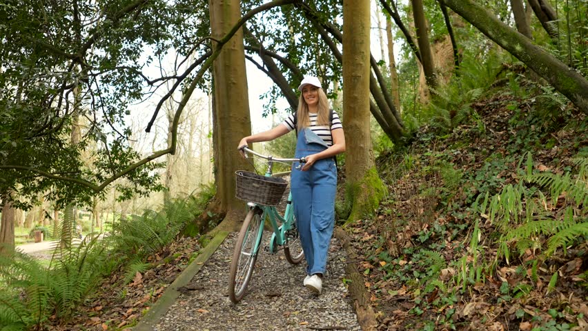 Woman walking with bicycle along park path, enjoying sunlight filtering through trees, embodying carefree summer leisure and outdoor wellness