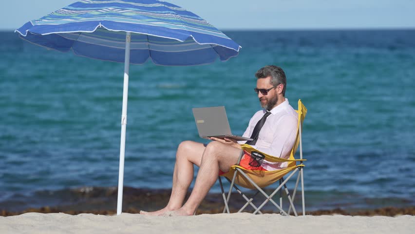 A business man work and fun on a summer beach. A freelancer typing on a laptop under the sun beach. A businessman on vacation, working remotely. A traveler working online by the ocean.