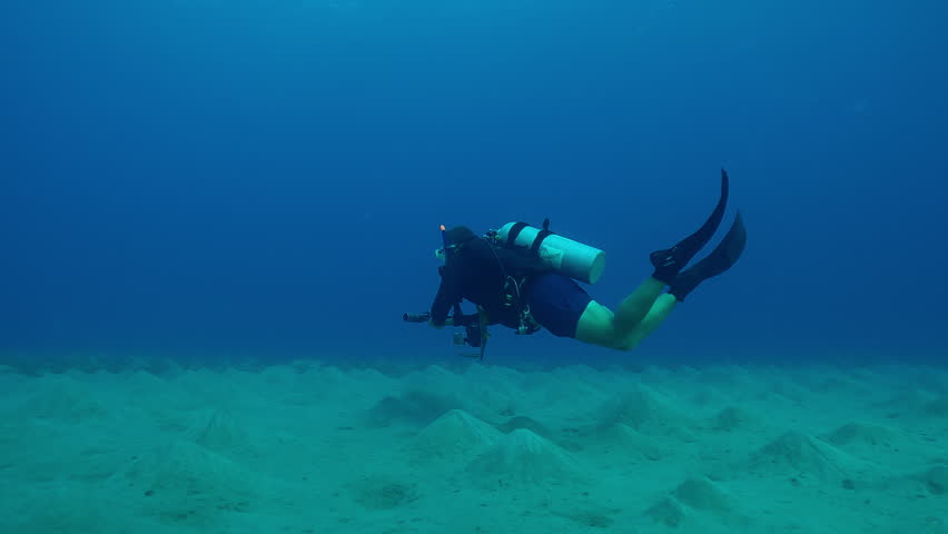 Lonely scuba diver cameraman swims above the sea bottom with sandy hills on the depth, Forward movement above hilly sand seabed on underwater desert of sea deep