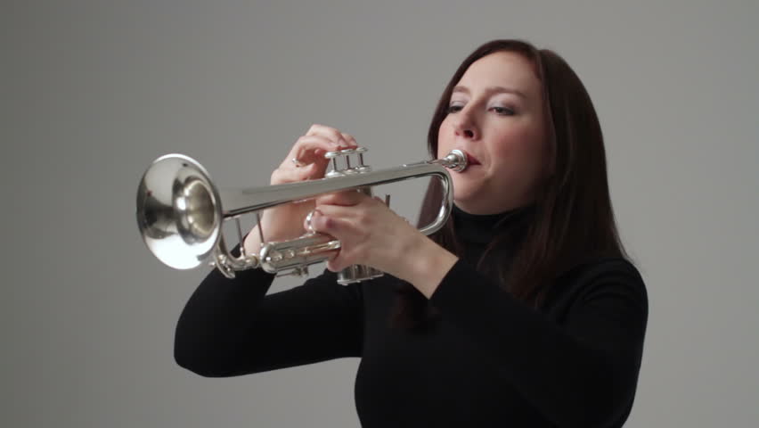 Young woman plays the trumpet in a studio. Mid shot.