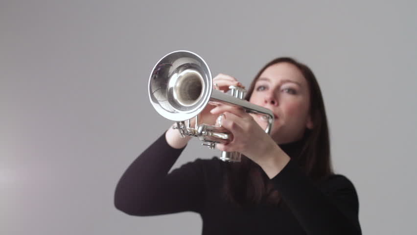 Young woman plays the trumpet in a studio. Close up with shallow focus and a