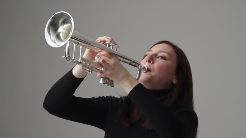 Young woman plays the trumpet in a studio. Mid shot with jib movement up at
