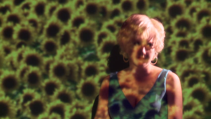 Blonde girl dances to unheard music in a projection of sunflowers. Mid shot.