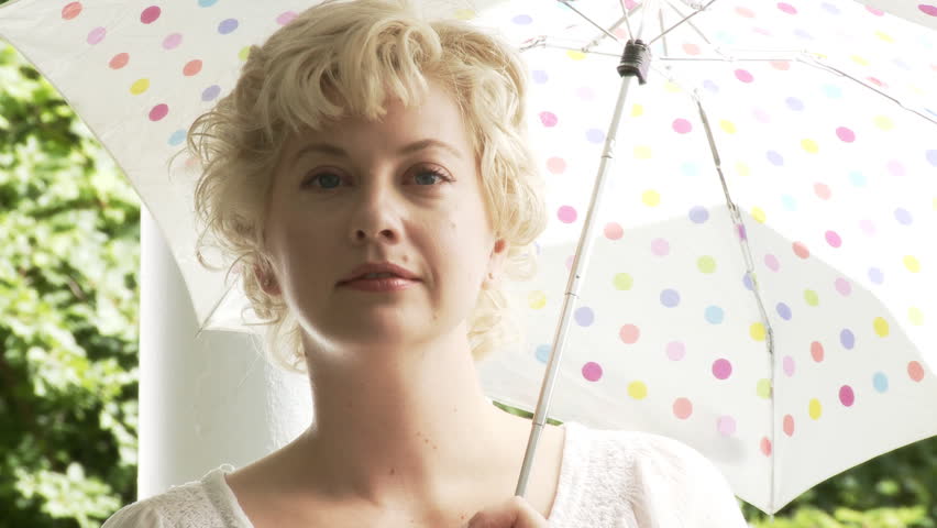 Close up of blonde girl with a polka dot parasol in bright summer sunshine.