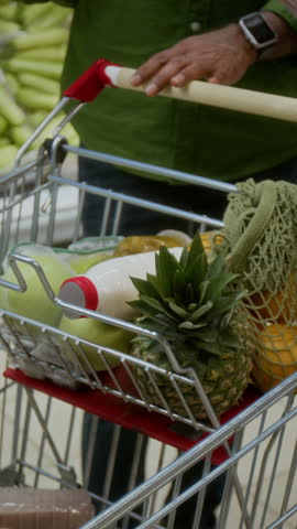 Vertical closeup shot of adult couple putting fresh vegetables in shopping cart at grocery store