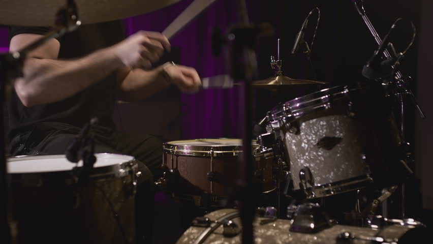 A young Caucasian man drummer plays in a music studio. Knocks the rhythm into the drum with sticks. Records a track of his rock band. Male hitting drum metal cymbals in repetition studio. Slow motion