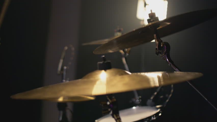 A young Caucasian man drummer plays a drum kit in a music studio. Creates music and art. Drum set, drum kit in dark, drummer plays. The rock band is rehearsing, studying. The musician is playing