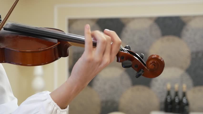 Close-up of a girl playing the violin. Close-up of hands playing the violin. A female violinist plays the violin at an evening performance.
