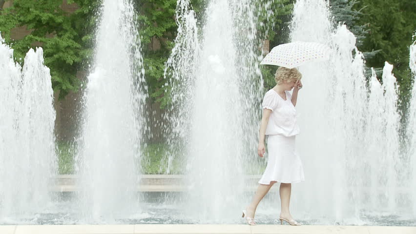 Girl poses with an umbrella in front of a fountain. Recorded in slow motion at