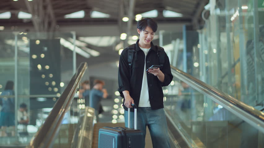 Happy asian man with backpack checking flight in phone on escalator in airport terminal, People concentrating typing digital device for travel in transportation, Concept of travel